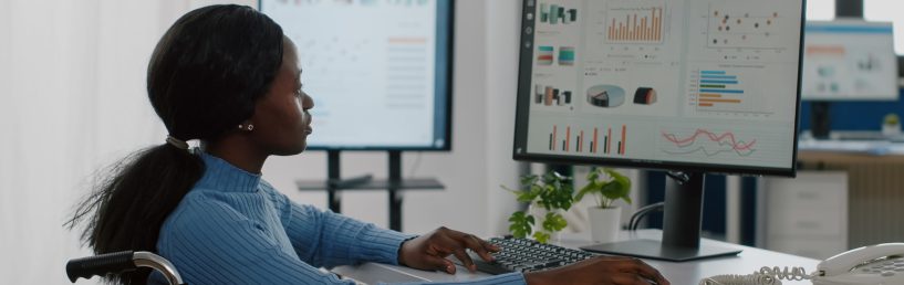 African disabled invalid manager woman working at pc showing data prosessing on desktop for project regarding economy looking at financial documents checking graphs, reading raports in business office